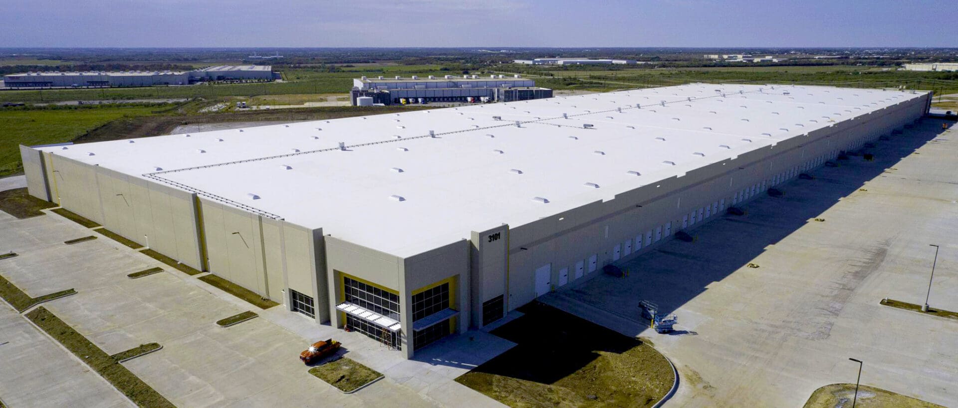 A large warehouse with many cars parked on the side.